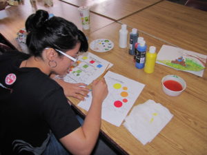 Estudiante de la Facultad pintando una hoja de papel con una actividad de niños. Esta pintando con acuarelas. Oprimir sobre la foto para información del Decanato de Asuntos Estudiantiles.